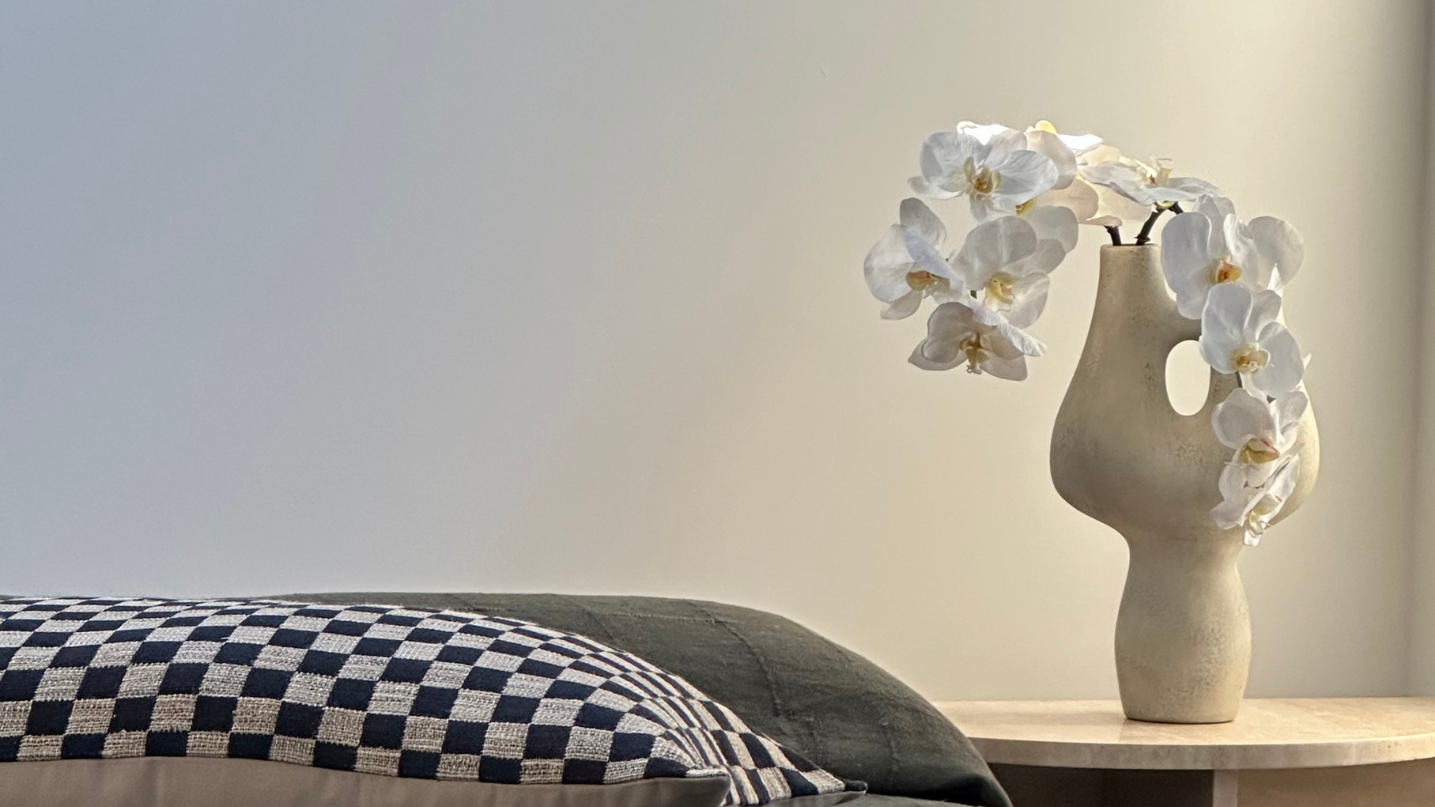 Elegant white orchids in a ceramic vase styled on a bedside table, adding a touch of timeless beauty and tranquility to the bedroom decor.